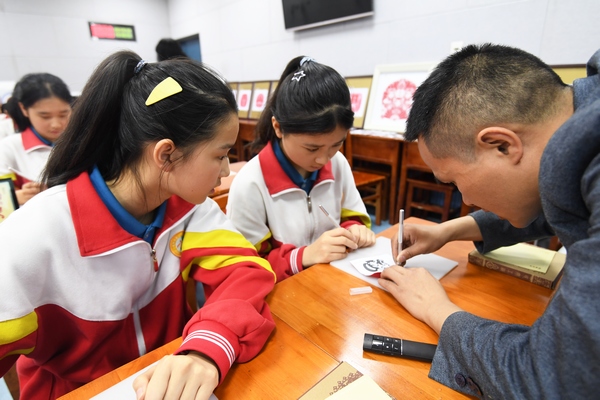 贵州省铜仁市非物质文化遗产传承人王再臣正在指导贵阳市第二十七中学的学生进行剪纸作品创作。
